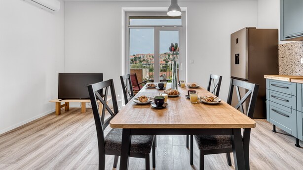 Cozinha moderna com mesa de jantar de madeira, cadeiras e vista para a cidade através de uma janela grande.