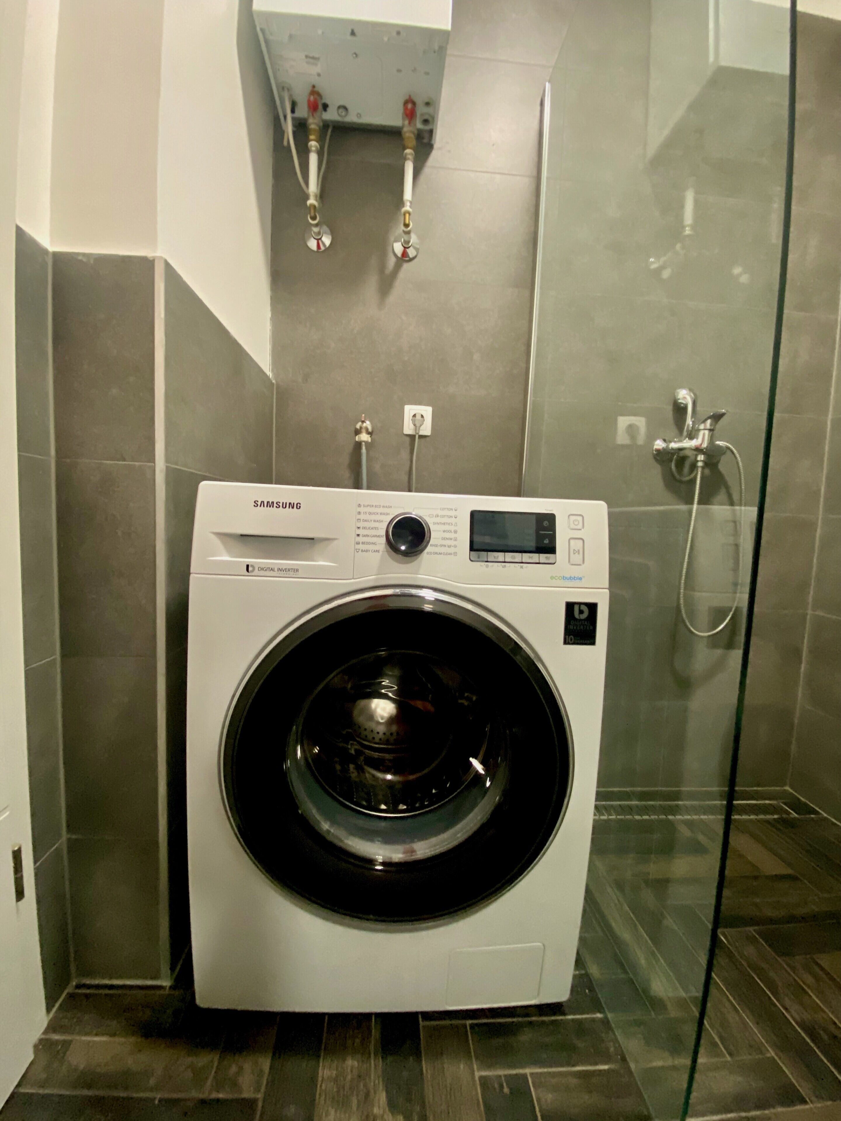 Une machine à laver Samsung dans une salle de bain équipée d’une douche en verre.