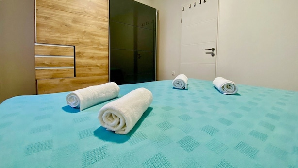 Ein Hotelzimmer mit einem Bett, zwei gerollten Handtüchern, einem Holzschrank und einer Tür zum Badezimmer.