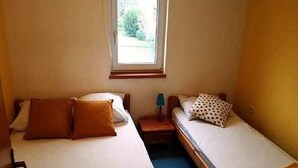 Un alojamiento pequeño, con una sola habitación, dos camas, un ventanal y una mesita de noche con lámpara.