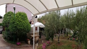Un espacio al aire libre cubierto con un banco de piedra, una sombrilla blanca y diversas plantas.