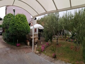 A covered outdoor area with a stone bench, a white umbrella, and various plants. - Apartments Marija - One Bedroom Apartment with Balcony and Sea View (Pirovac)