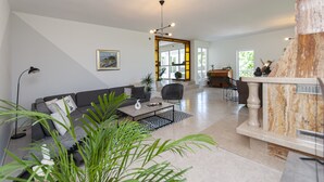 A modern living room with a sofa, coffee table, and a fireplace. There is a staircase leading to another level, and a large window providing natural light. - Villa Green Castle - Five bedroom villa with swimming pool (Zadvarje)
