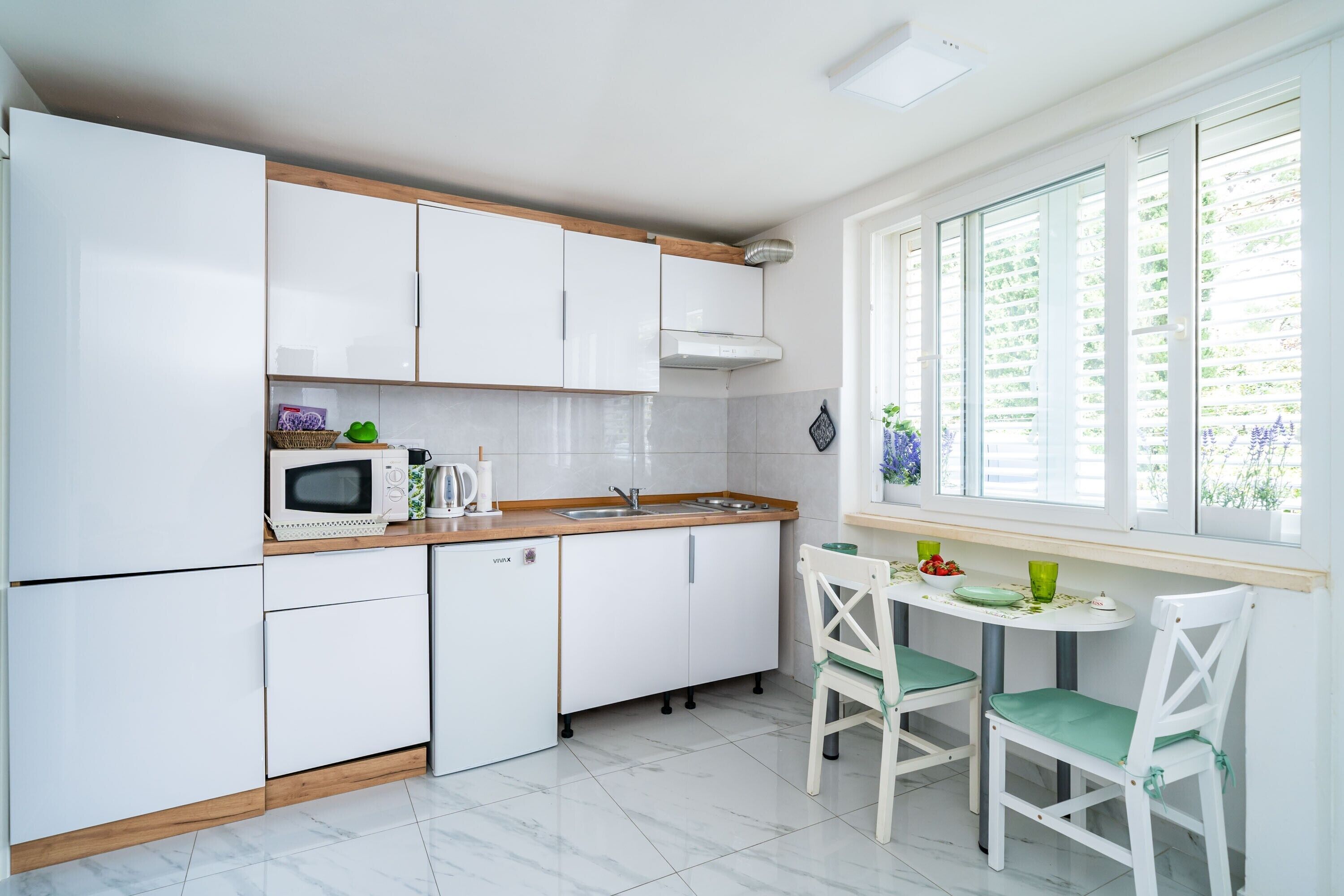 A kitchen with white cabinets, a microwave, a sink, and a window with blinds.