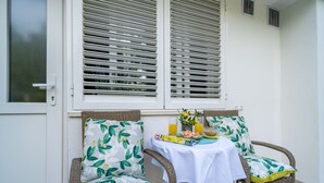 A wicker chair with a floral cushion, a small table with a white tablecloth, and a window with white shutters. - Apartment Laneta - Studio Apartment with Terrace (Dubrovnik)