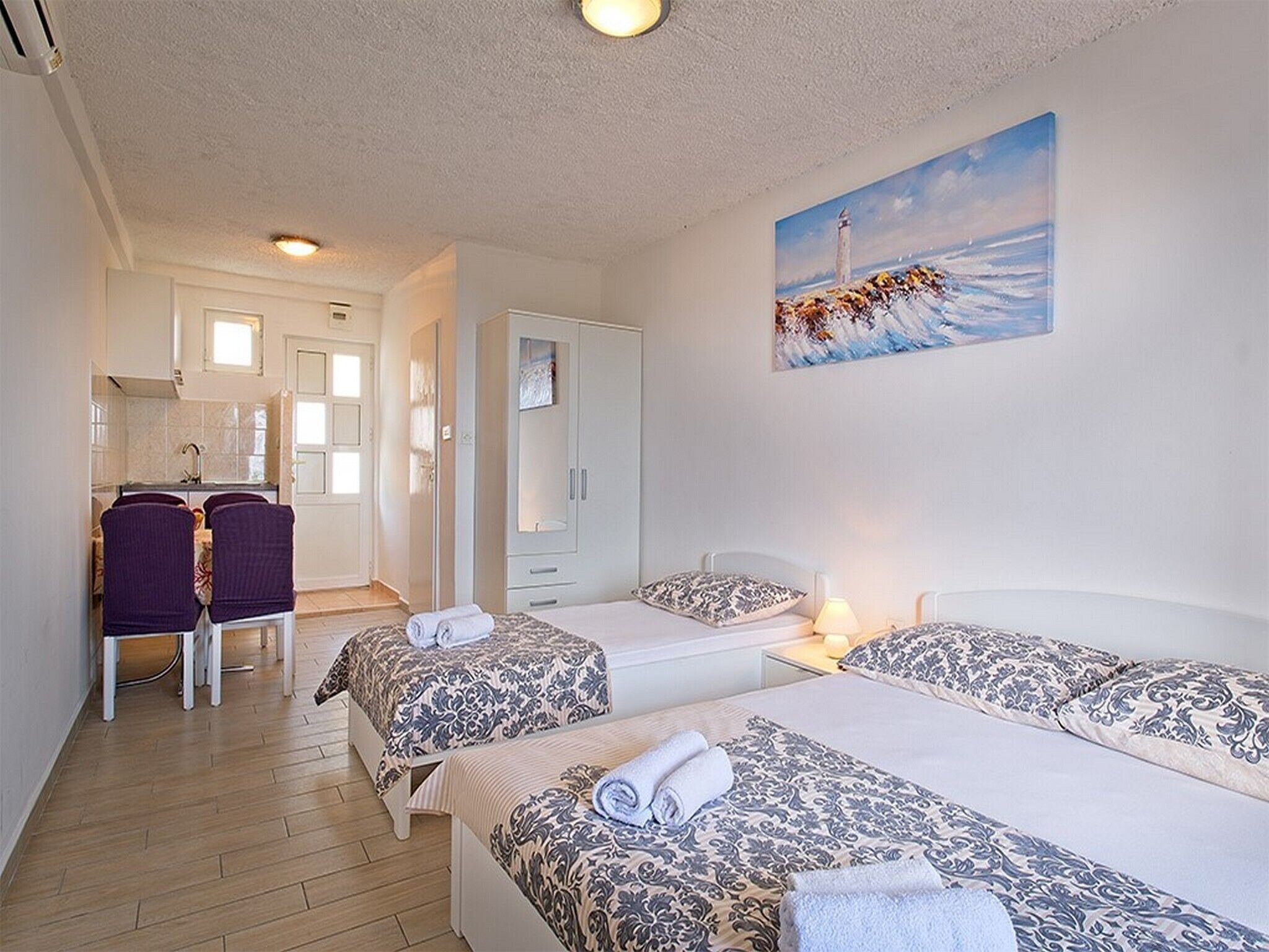 A hotel room with two beds, a desk, and a chair. There is a painting of a lighthouse on the wall.