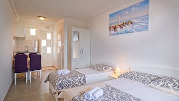 A hotel room with two beds, a desk, and a chair. There is a painting of a lighthouse on the wall.