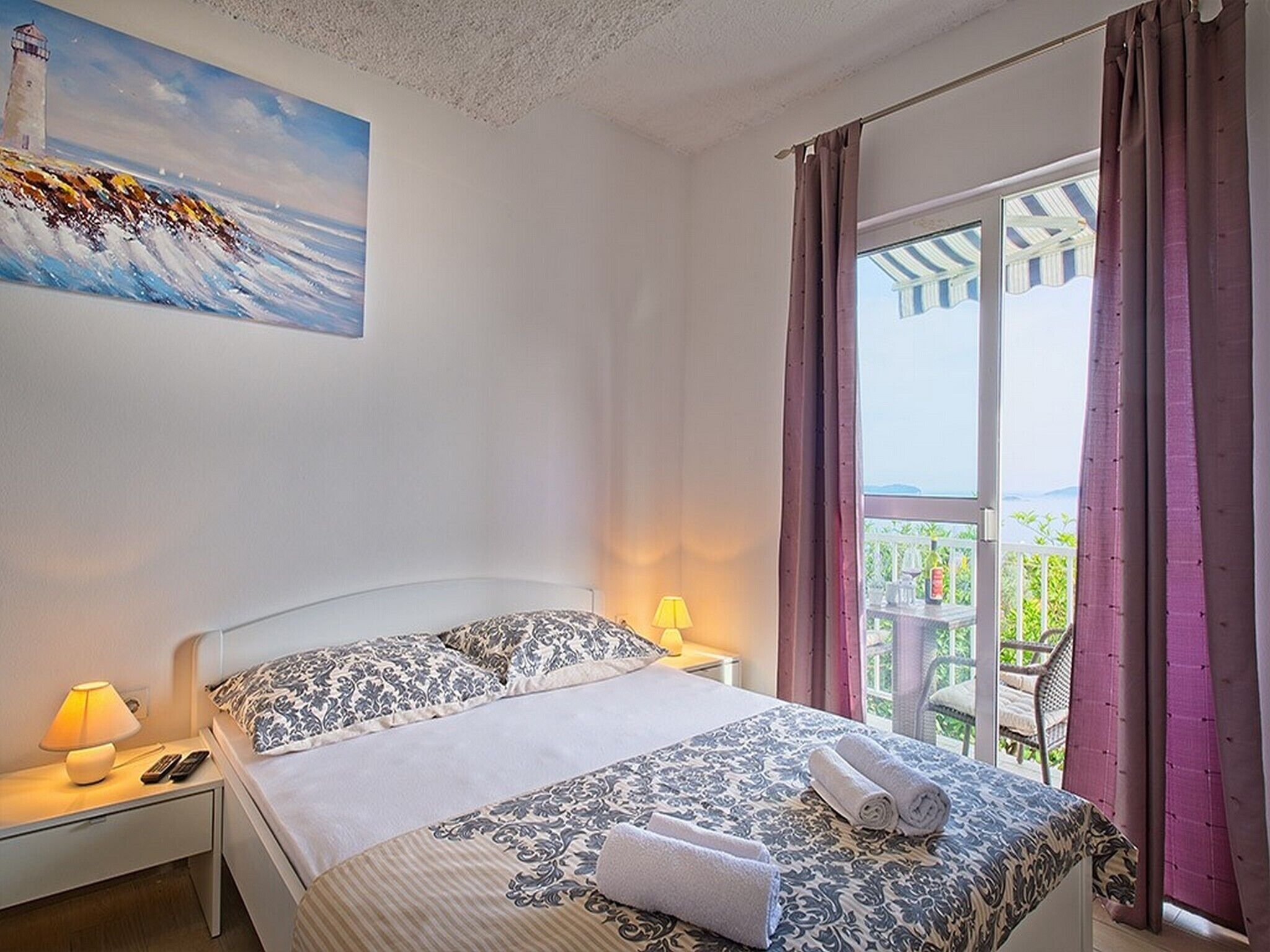 Habitación de hotel con cama, mesitas de noche, un cuadro y un balcón con cortinas.