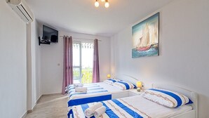Habitación de hotel con dos camas, televisión, un cuadro y balcón con cortinas.
