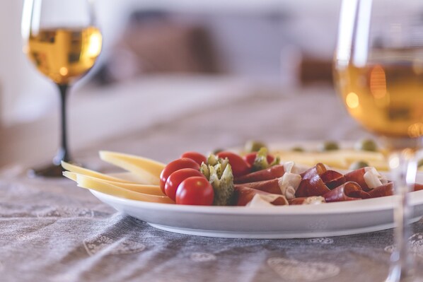 A plate of food with cheese, tomatoes, and meat, and two glasses of wine on a table.