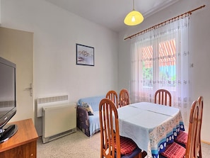 A cozy room with a bed, a table, and chairs. There's a radiator, a television, and a window with curtains.