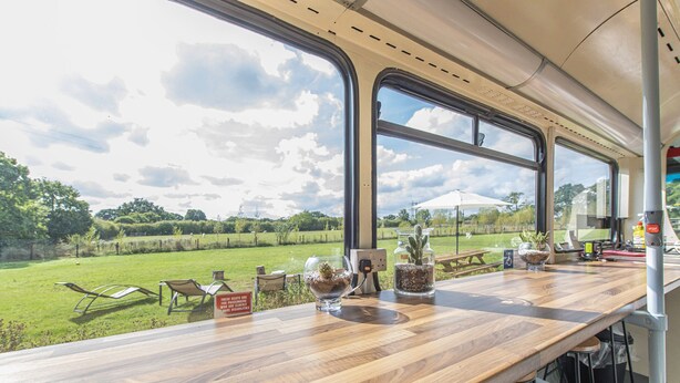 A wooden bar with large windows overlooking a grassy field and picnic area. - Double Decker Bus on an Alpaca Farm Sleeps 8 (Newton Abbot)