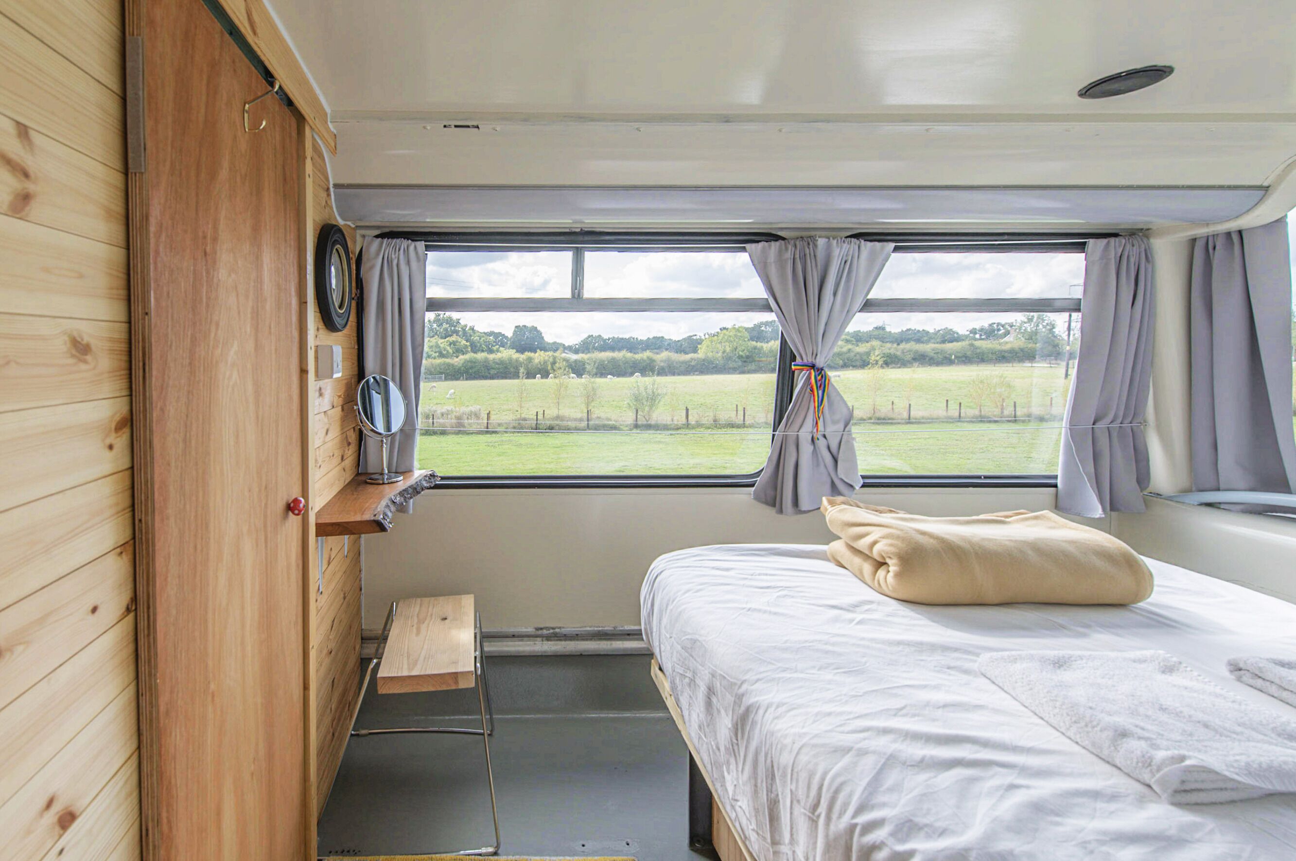 Un dormitorio con cama, un armario de madera, un espejo y una ventana con cortinas.
