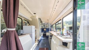 A narrow corridor with a kitchenette on one side, a counter with various items on the other, and emergency pull handles. - Double Decker Bus on an Alpaca Farm Sleeps 8 (Newton Abbot)