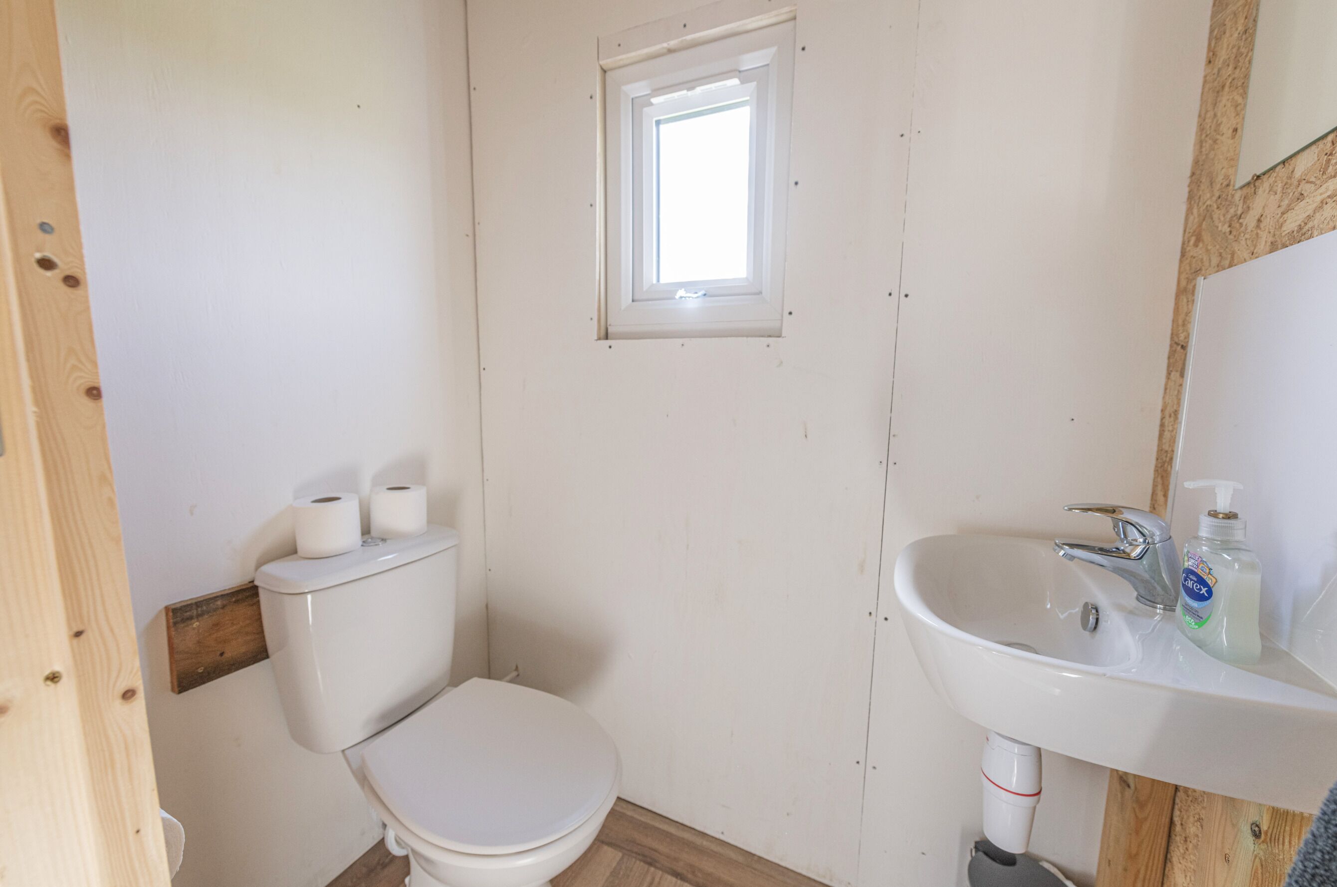 Une petite salle de bain simple, équipée de toilettes, d’un lavabo et d’une fenêtre.