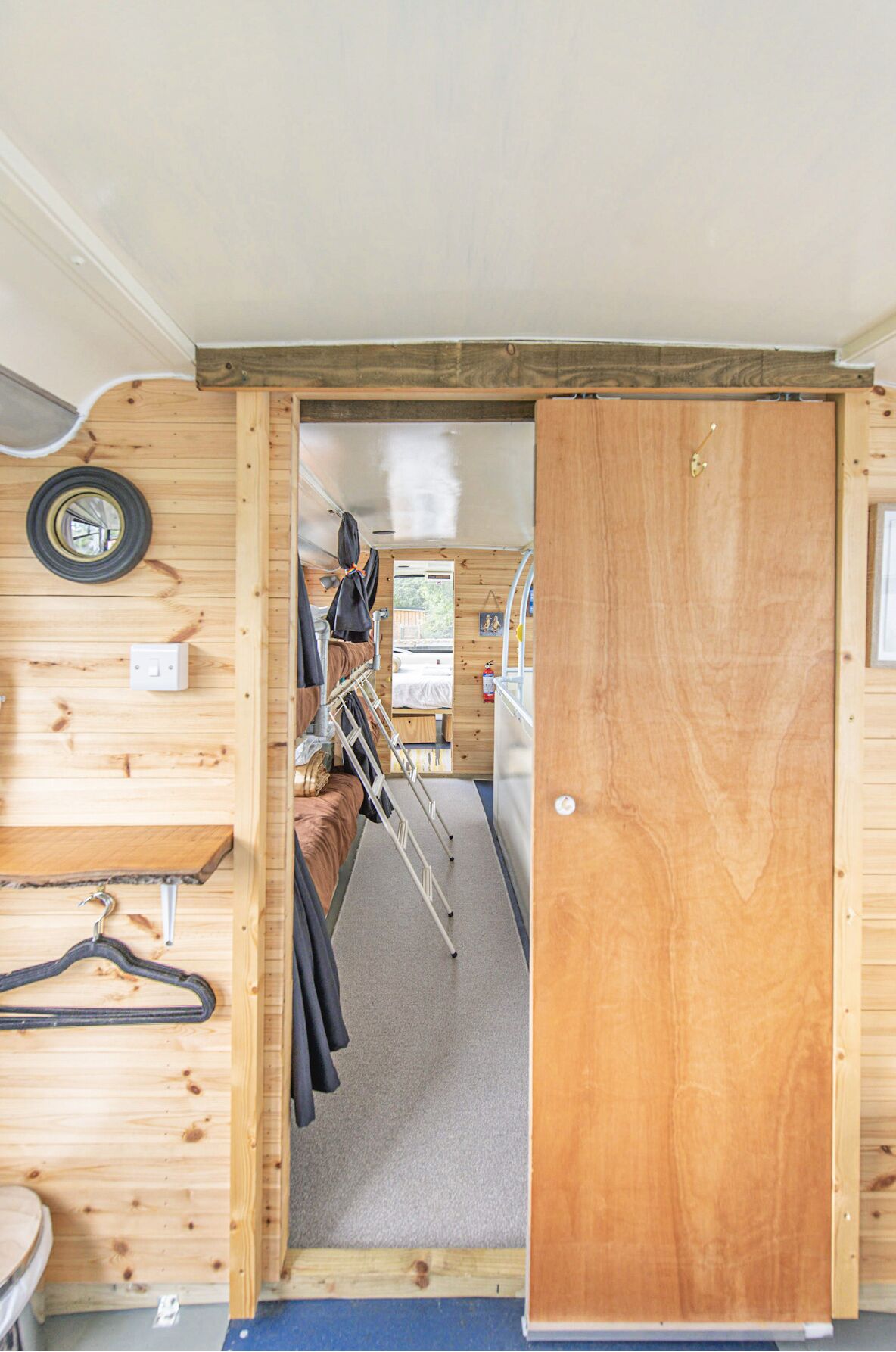 A compact, wooden interior with a bed, a small table, and a wall-mounted tire.