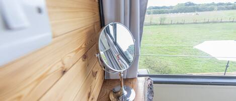 A wooden wall with a mirror reflecting a window view of a grassy field and a fence.