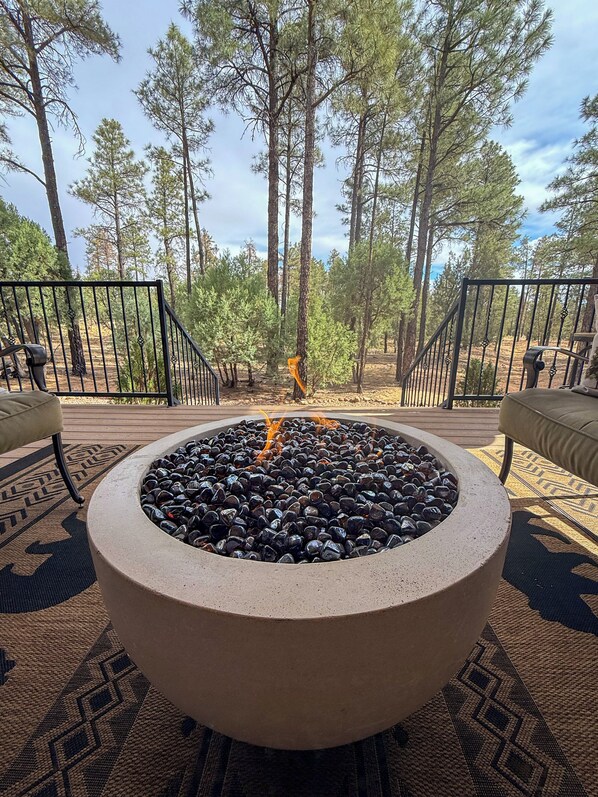 A circular fire pit surrounded by a patterned rug, with a view of tall pine trees in the background.