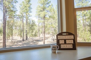 A window with a view of a forest, a welcome sign, and a mug on the windowsill.
