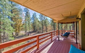 A wooden deck with a swing chair and a blue cushion, overlooking a forested area.