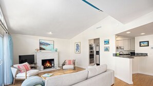 Un salon moderne doté d’une cheminée, d’un canapé, d’un téléviseur et d’un coin cuisine avec des placards et des appareils électroménagers.