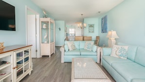 Una sala de estar con un sofá azul claro, un mueble blanco y una mesa de centro de mimbre.