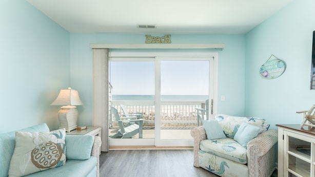Una habitación con vista a la playa, que incluye un sofá, una silla, una lámpara y un armario.