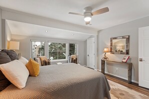 A bedroom with a large bed, a ceiling fan, a window with a view of trees, and a wooden console table with a lamp. - Villas of Aspen by Snowmass Vacations (Aspen)