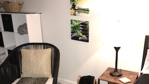 A room with a black chair, a woven rug, a small wooden nightstand with a lamp, and wall art depicting nature. - Glamping with a twist (Jacksonville)