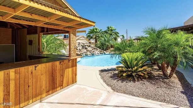 A wooden bar area with a pool and palm trees.