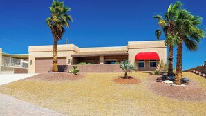 A modern building with a red awning, palm trees, and a gravel driveway.