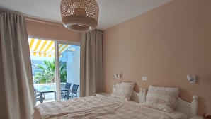 A bedroom with a large bed, a bedside table, a hanging light fixture, and a view of the outside balcony. - Sunny apartment with sea view (Mogán)