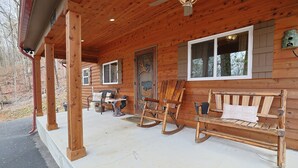 A wooden cabin with a porch, rocking chairs, a table, and a bench. - Couples Retreat Cabin w HotTub & EV Charger Bryson (Bryson City)