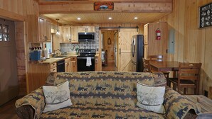 A cozy cabin interior with a wooden interior, a sofa with animal prints, a kitchen with a stove and microwave, and a dining area with a table and chairs. - Couples Retreat Cabin w HotTub & EV Charger Bryson (Bryson City)