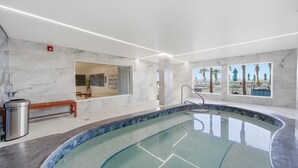 En modern inomhuspool med väggar i marmor, en bänk och utsikt över palmer.