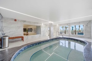 Une piscine intérieure moderne avec des murs en marbre, un banc et une vue sur des palmiers.