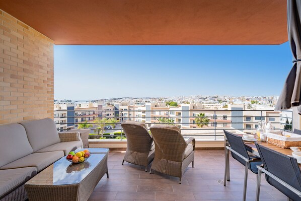A balcony with wicker furniture, a table with fruit, and a city view.