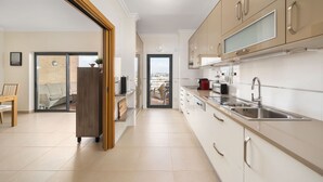 Une cuisine moderne avec des armoires blanches, des appareils en acier inoxydable et une vue sur l’extérieur, visible à travers la porte.