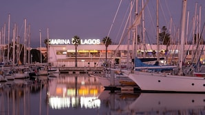 Un port de plaisance où sont amarrés de nombreux bateaux, un bâtiment portant l’inscription « MARINA LAGOS » en arrière-plan, et des reflets sur l’eau.