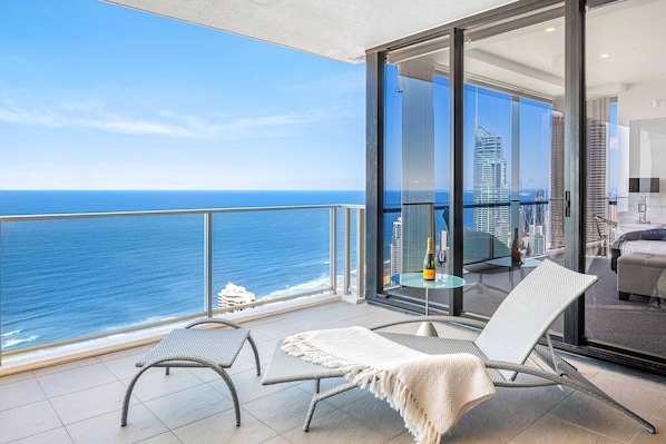 Enjoy ocean views and city skyline vistas from this spacious balcony with a glass door leading to a seating area.