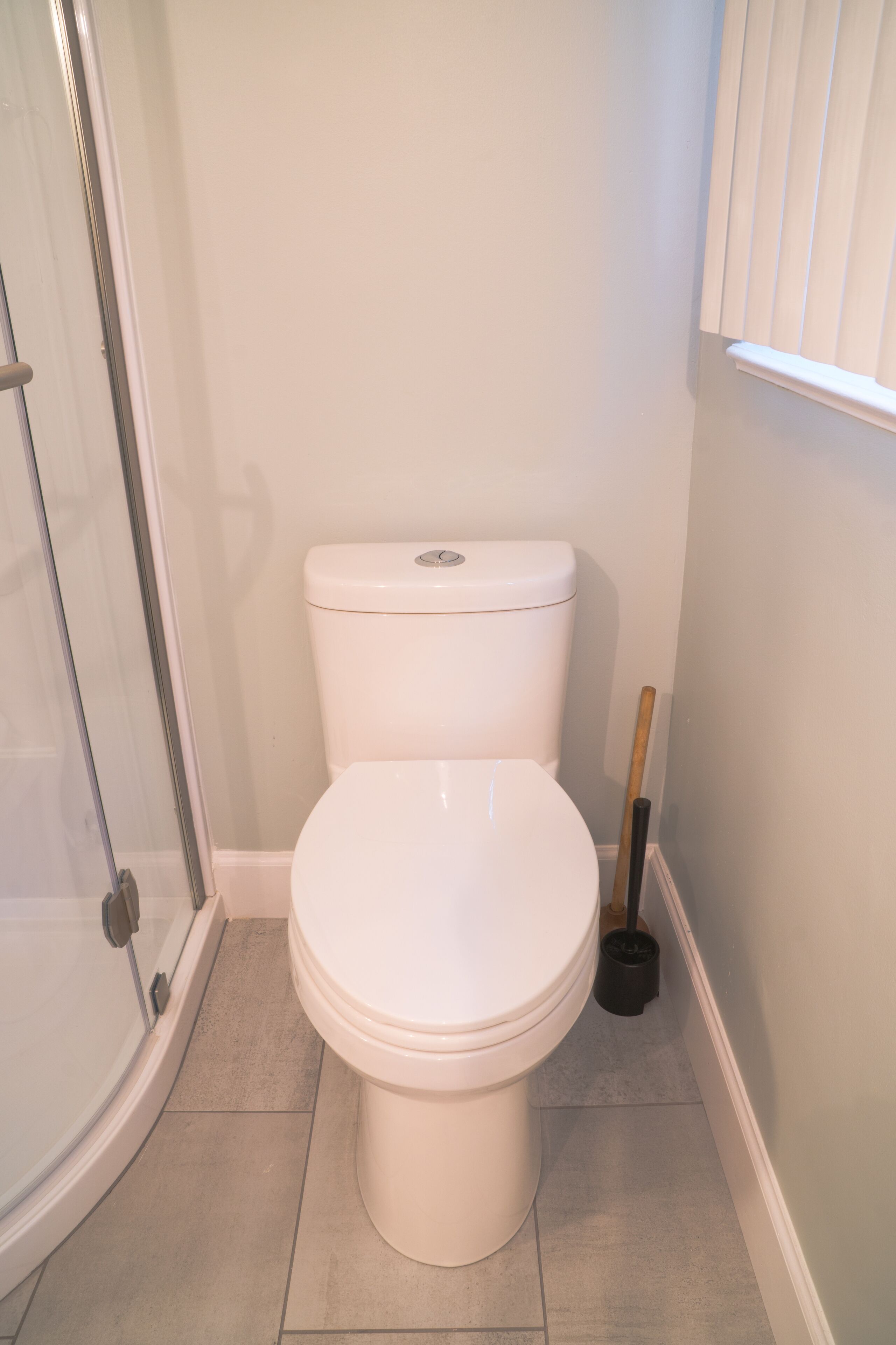 A bathroom with a white toilet, a glass shower enclosure, and a black cleaning brush.