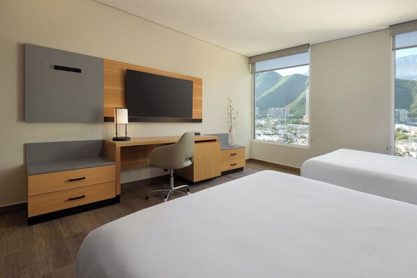 A hotel room with a bed, a desk, a chair, a TV, and a view of a city and mountains. - Hyatt Place Monterrey Valle (San Pedro Garza García)