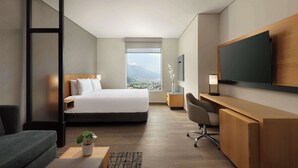 Ett modernt hotellrum med en stor säng, ett skrivbord, en TV och utsikt över staden.