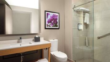 Un baño moderno con ducha de vidrio, lavamanos blanco y un cuadro enmarcado con flores.