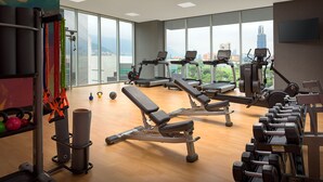 Ett gym med träningsutrustning, stora fönster och utsikt över staden.