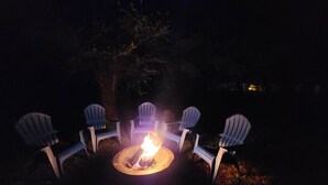 A nighttime outdoor seating area with four Adirondack chairs arranged around a central fire pit. - Luxurious beds, remodeled, very clean, quiet neighborhood, big backyard & tree!! (Denison)