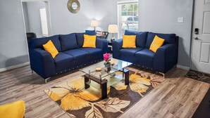 A living room with two dark blue sofas, yellow cushions, a glass coffee table, and a floral rug. - Luxurious beds, remodeled, very clean, quiet neighborhood, big backyard & tree!! (Denison)
