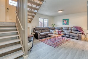 Ein geräumiges Wohnzimmer mit einem braunen Ledersofa, einer Holztreppe und einem farbenfrohen Teppich.