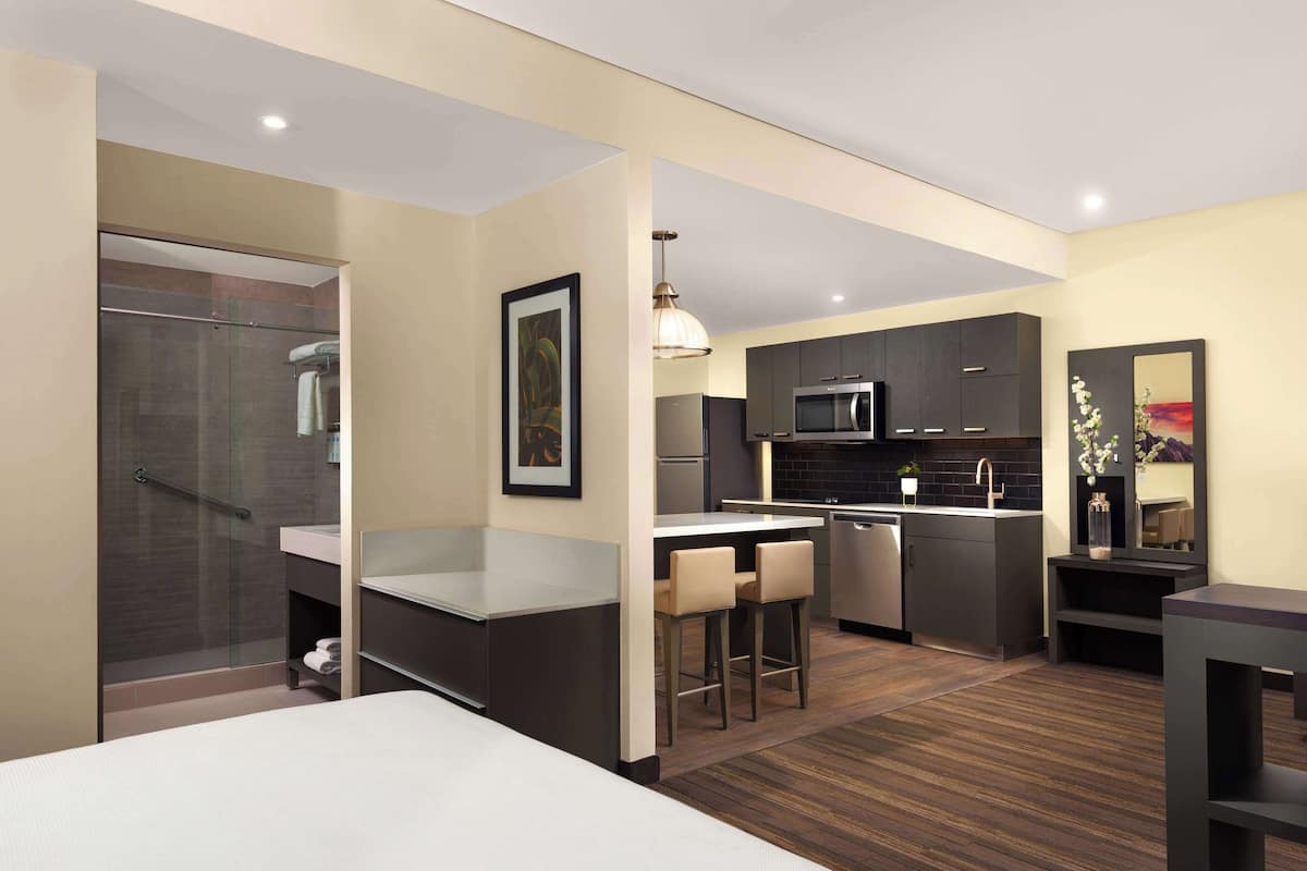 A modern hotel room with a separate kitchenette, a shower area, and a dining space with bar stools.
