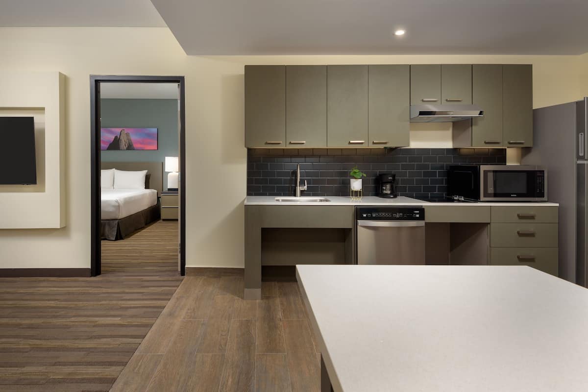 A modern hotel room with a kitchenette, a bed, a TV, and a bathroom.